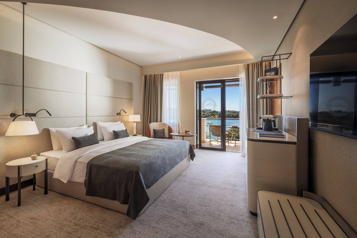 Ein modernes Hotelzimmer mit einem großen Bett, Nachttischen, einem Schreibtisch und einem Balkon mit Blick.