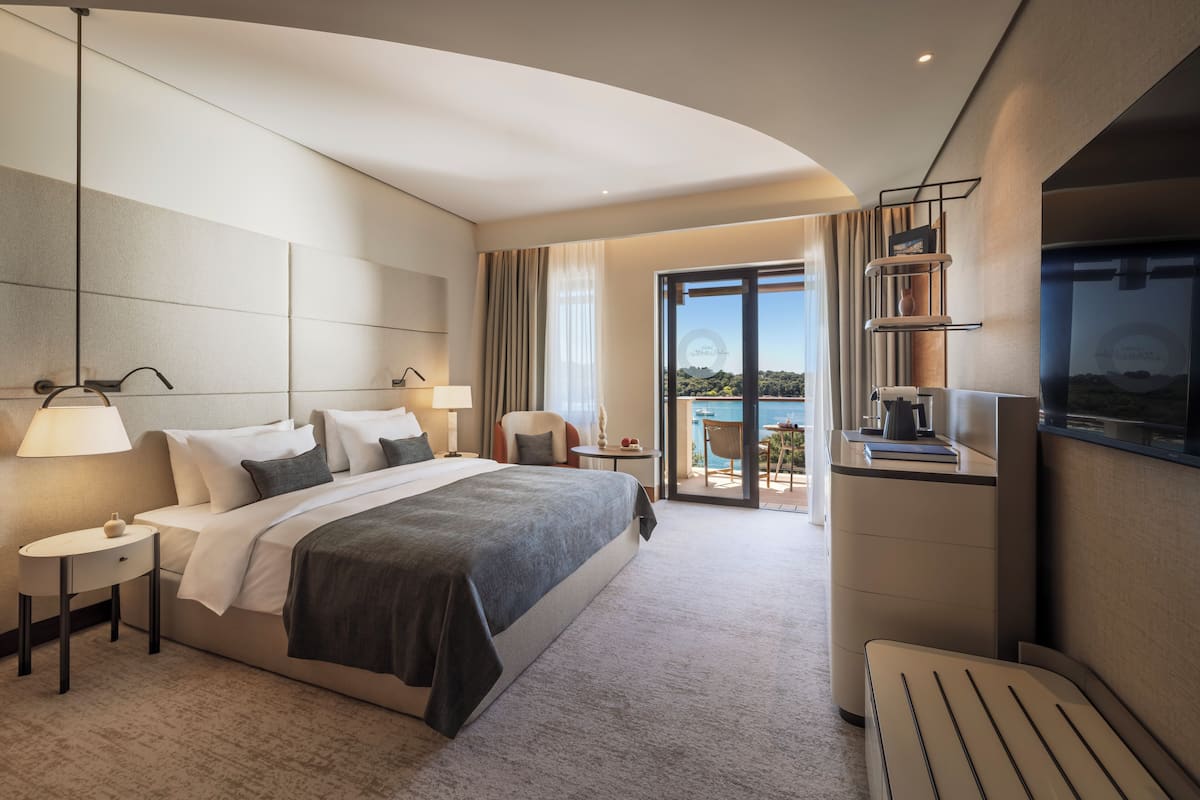 A modern hotel room with a large bed, bedside tables, a desk, and a balcony with a view.
