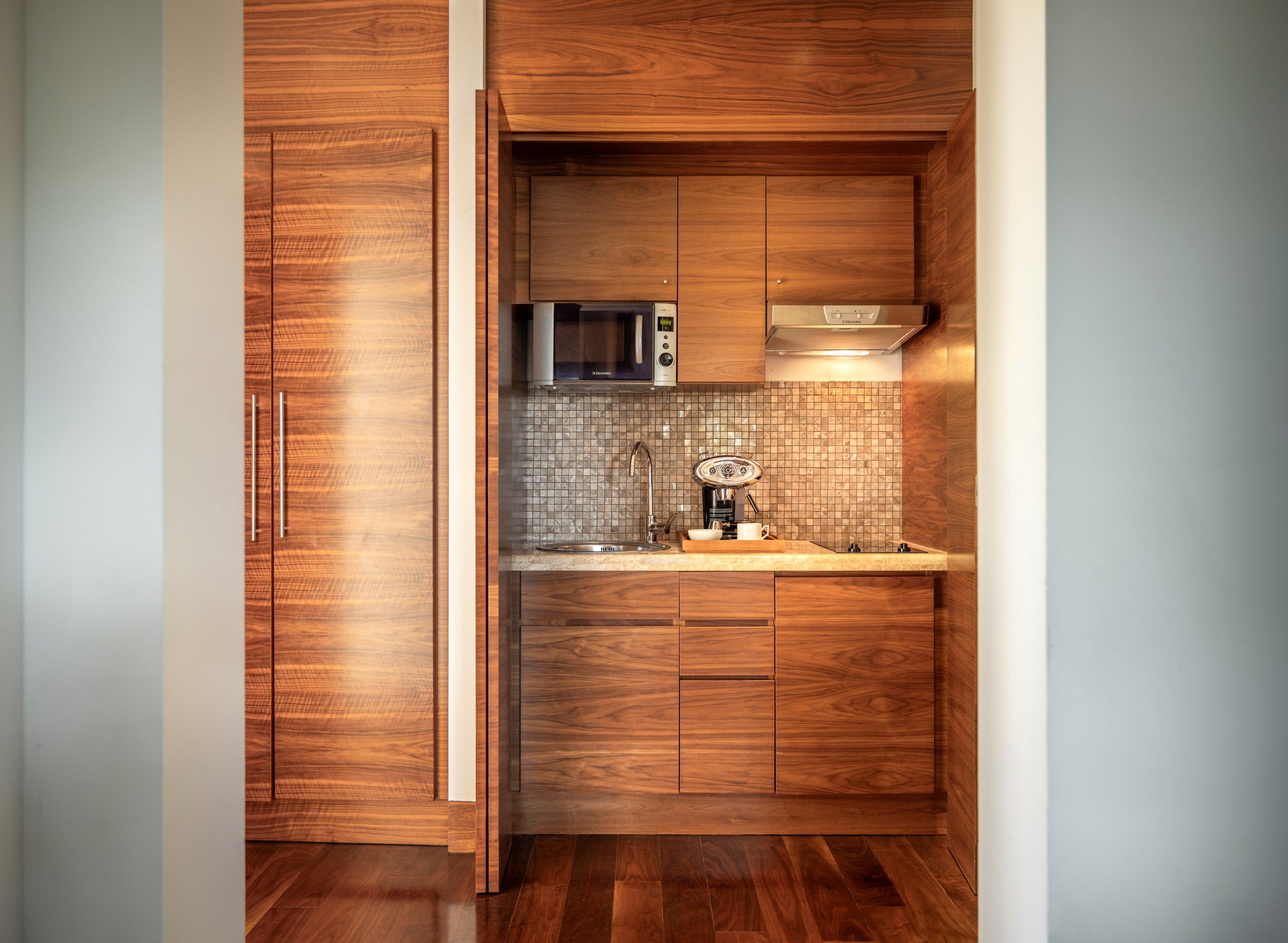 A compact kitchen with wooden cabinetry, a microwave, a coffee machine, and a tiled backsplash.