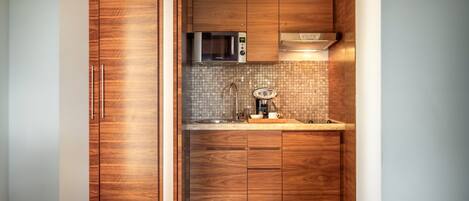 A compact kitchen with wooden cabinetry, a microwave, a coffee machine, and a tiled backsplash.
