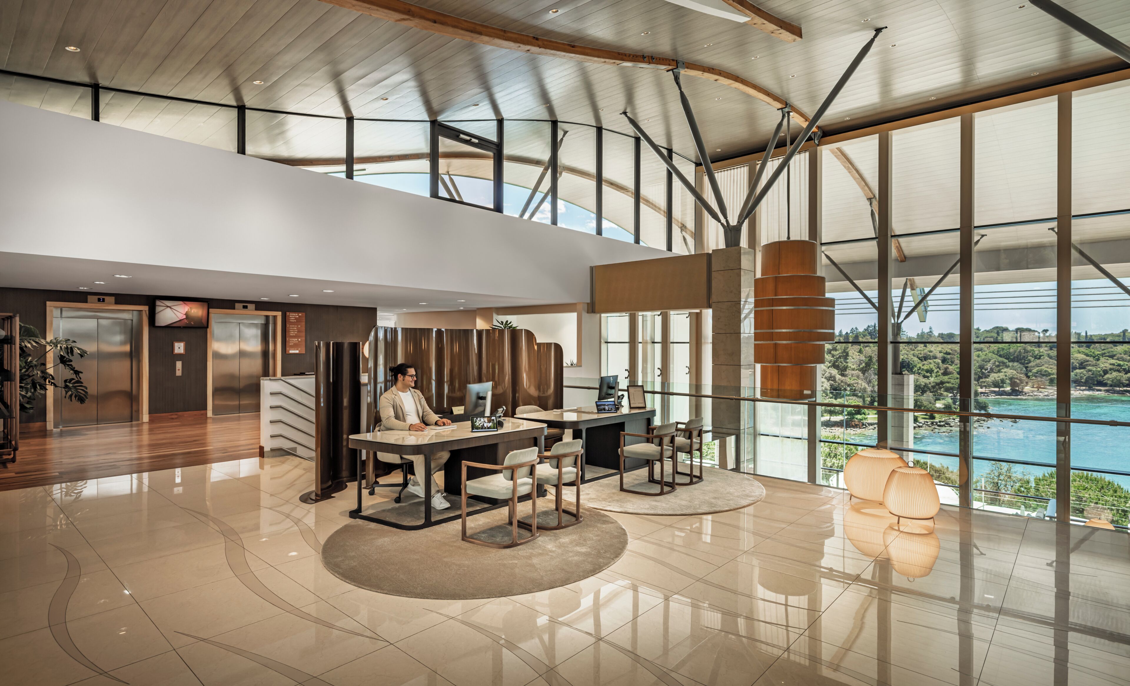 A spacious lobby with a high ceiling, modern furniture, and large windows offering a view of the outdoors.