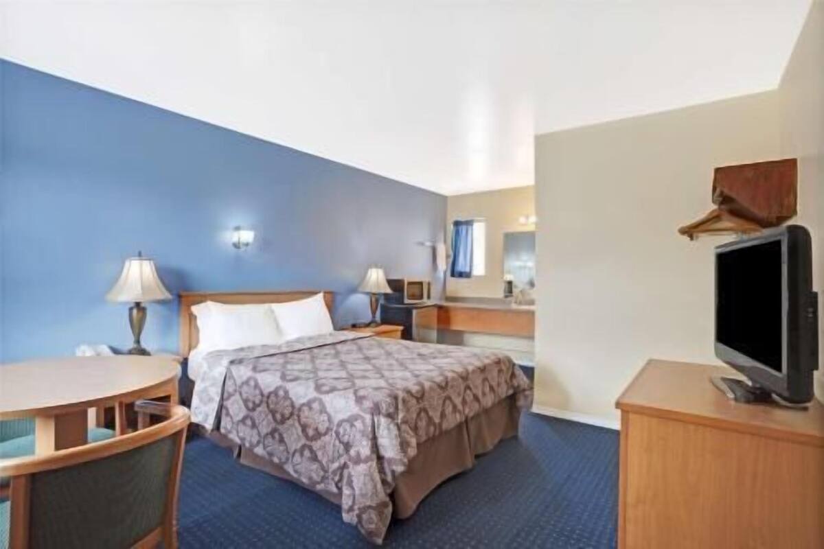 A hotel room with a bed, bedside tables, a desk, a chair, a TV, and a mirror.