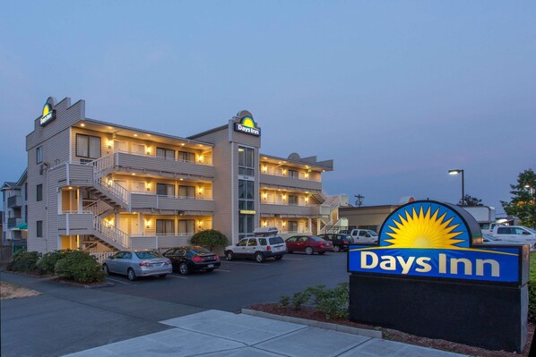 A Days Inn hotel with a multi-story structure, a parking lot, and a clear sky. - Days Inn by Wyndham Seattle North of Downtown (Seattle)