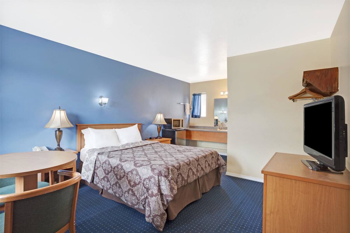 A hotel room with a bed, bedside tables, a desk, a chair, a television, and a mirror.