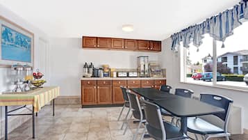 A kitchen with wooden cabinets, a dining table with chairs, a window with curtains, and a view of houses outside.