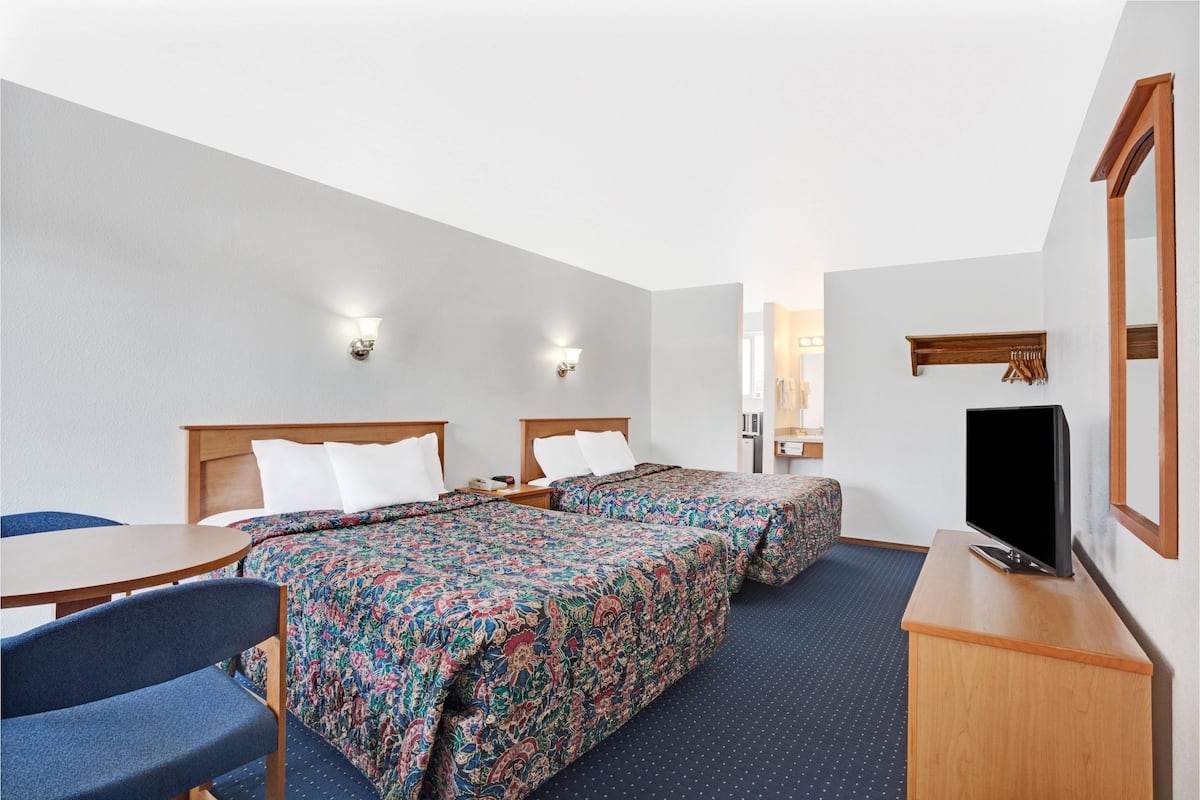 A hotel room with two beds, a desk, a chair, a television, and a mirror.