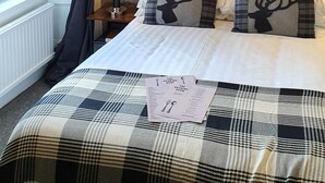 Habitación de hotel con cama, mesita de noche, lámpara y ventana con cortinas.
