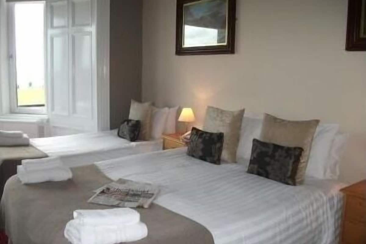 A hotel room with two beds, a window, a painting, and a lamp.