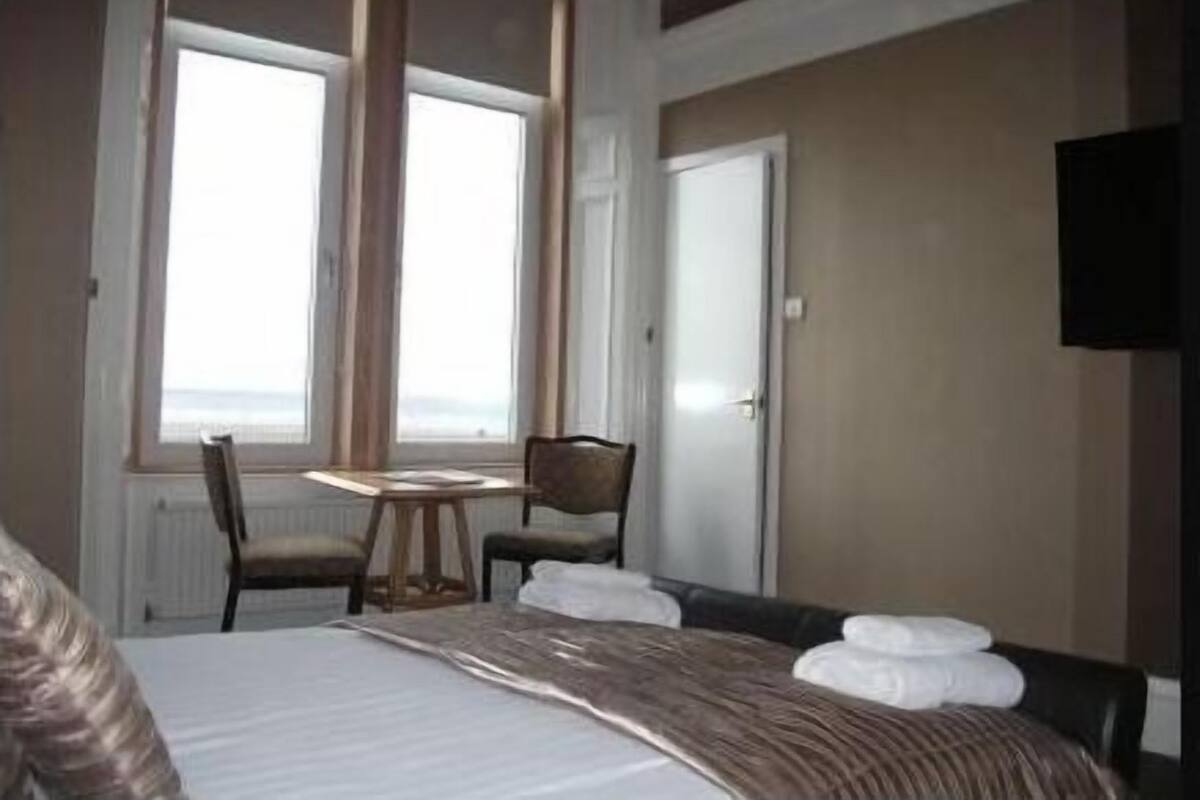 A hotel room with a bed, a small table, two chairs, a television, and a large window with a view.
