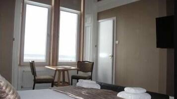 Quarto de hotel com cama, uma pequena mesa, duas cadeiras, televisão e uma janela grande com vista.