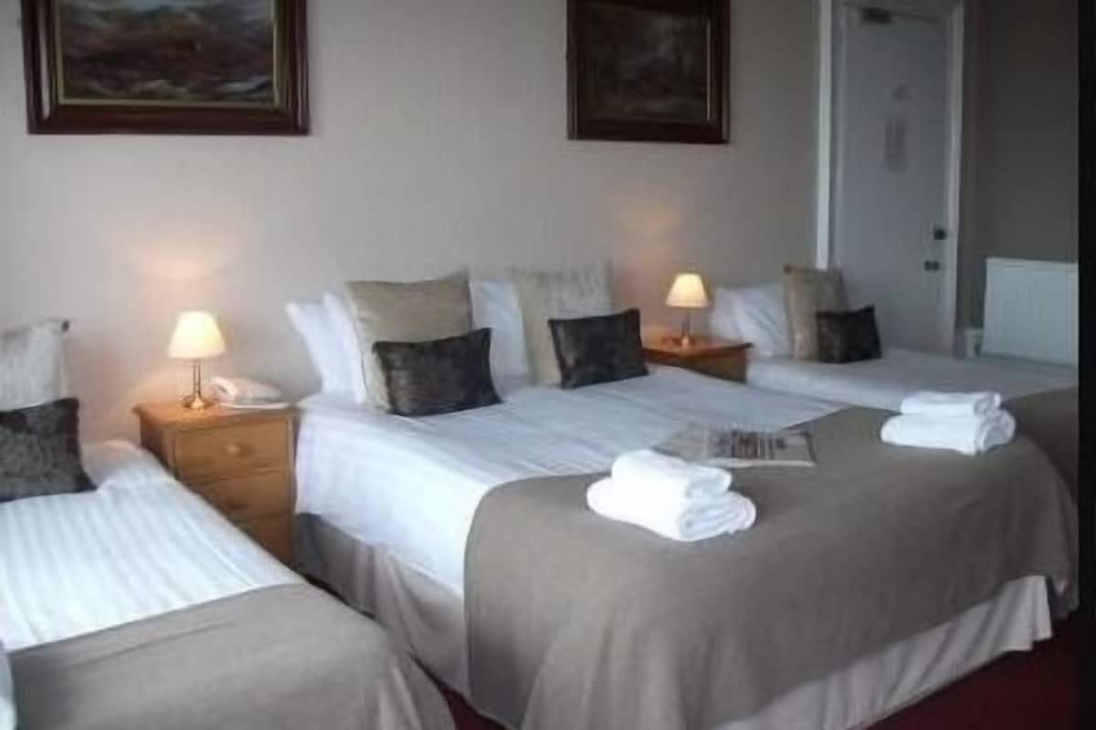 A hotel room with two single beds, a double bed, and a small table with a lamp.