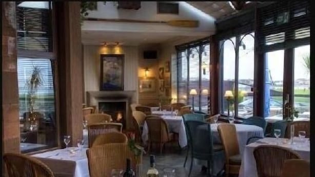 Interior de restaurante con mesas redondas, sillas de mimbre y una chimenea.