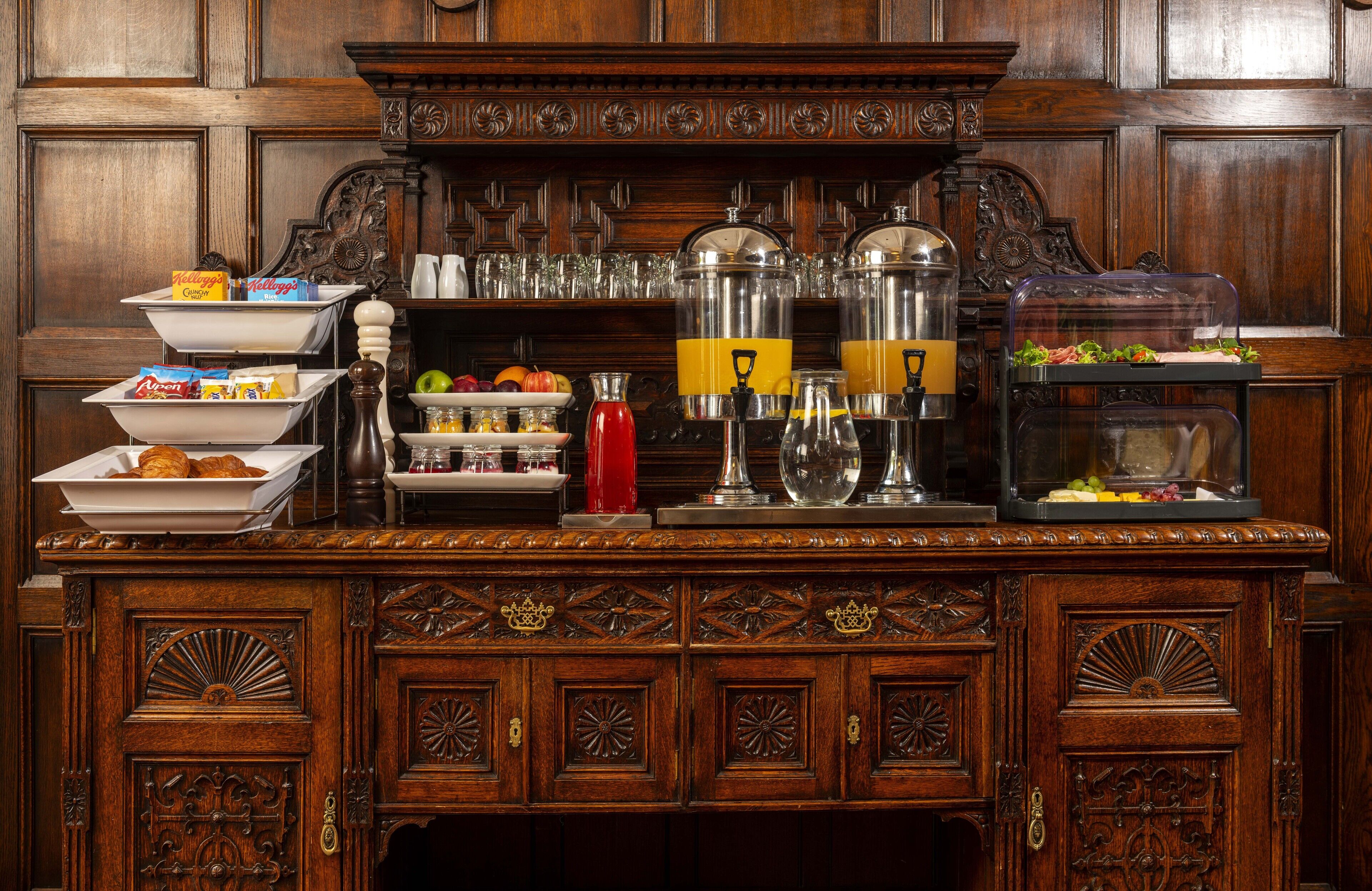 A buffet setup with various food items and beverages on a wooden counter with intricate carvings.