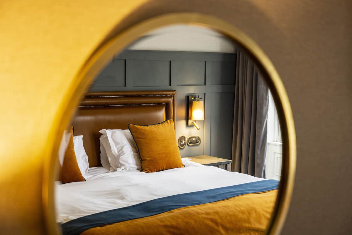 A hotel room with a large bed, a headboard, a nightstand, and a wall-mounted lamp.