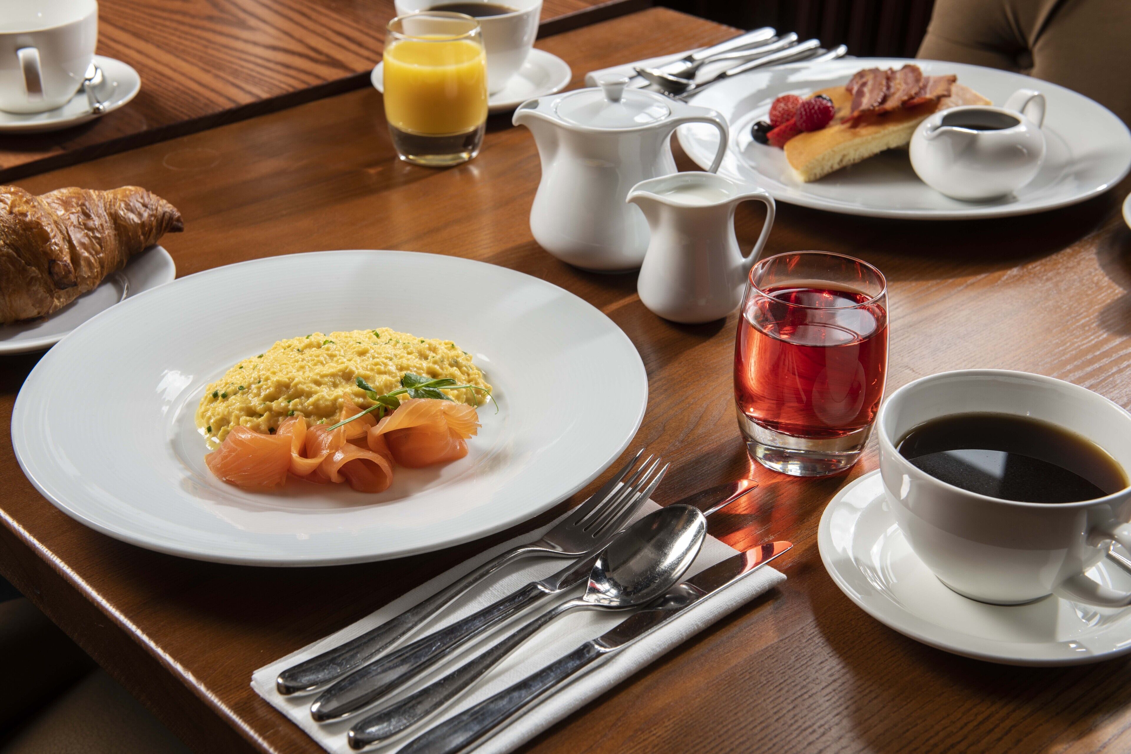 A breakfast setting with plates of food, a croissant, a cup of coffee, and a glass of juice.