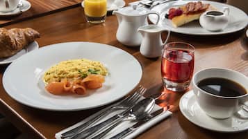 A breakfast setting with plates of food, a croissant, a cup of coffee, and a glass of juice.
