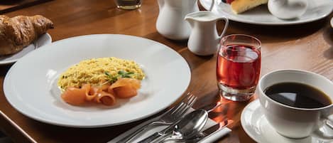 A breakfast setting with plates of food, a croissant, a cup of coffee, and a glass of juice.