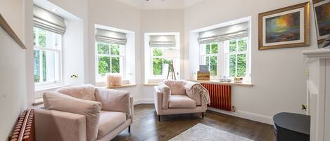 A spacious living room with a high ceiling, large windows, a fireplace, and a cozy seating area.