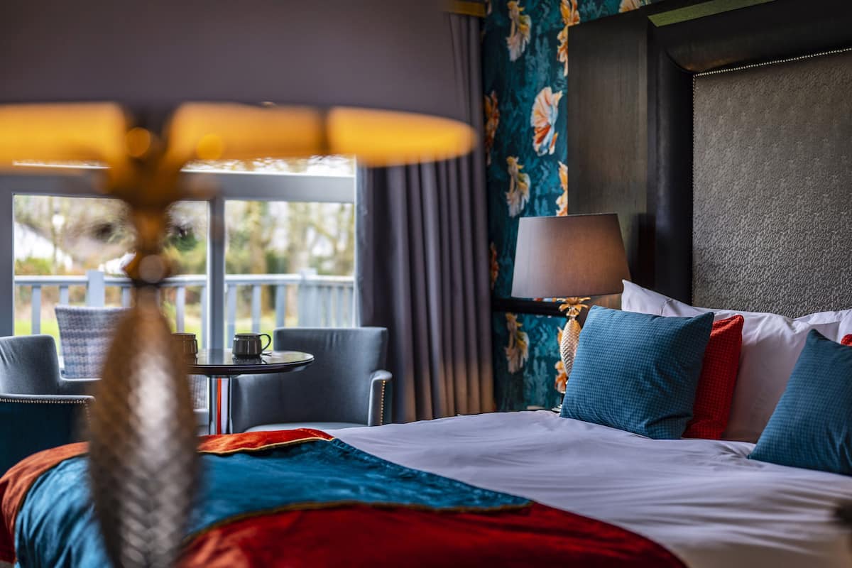 A hotel room with a bed, a table with a lamp, a chair, and a view of the outdoors.