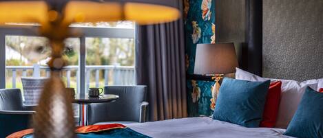 A hotel room with a bed, a table with a lamp, a chair, and a view of the outdoors.