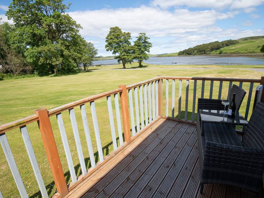 A deck with a wooden railing overlooking a grassy area with trees and a lake.