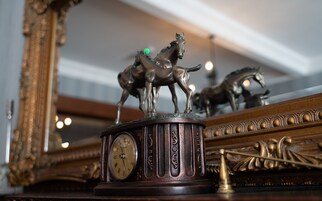 Um relógio com algarismos romanos e uma estatueta de cavalo em cima.