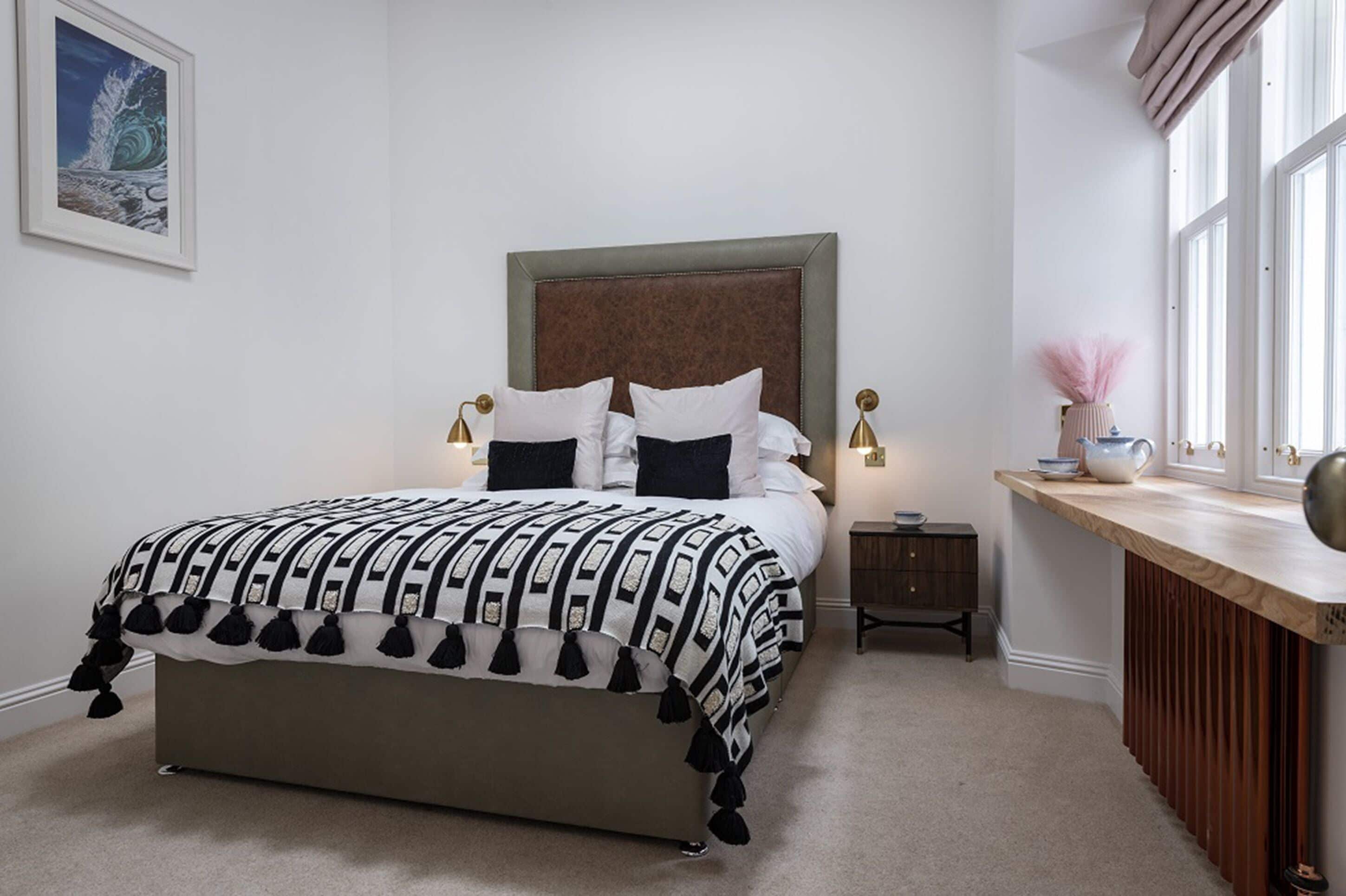 A bedroom with a bed, bedside tables, a nightstand, a window with curtains, and a painting on the wall.