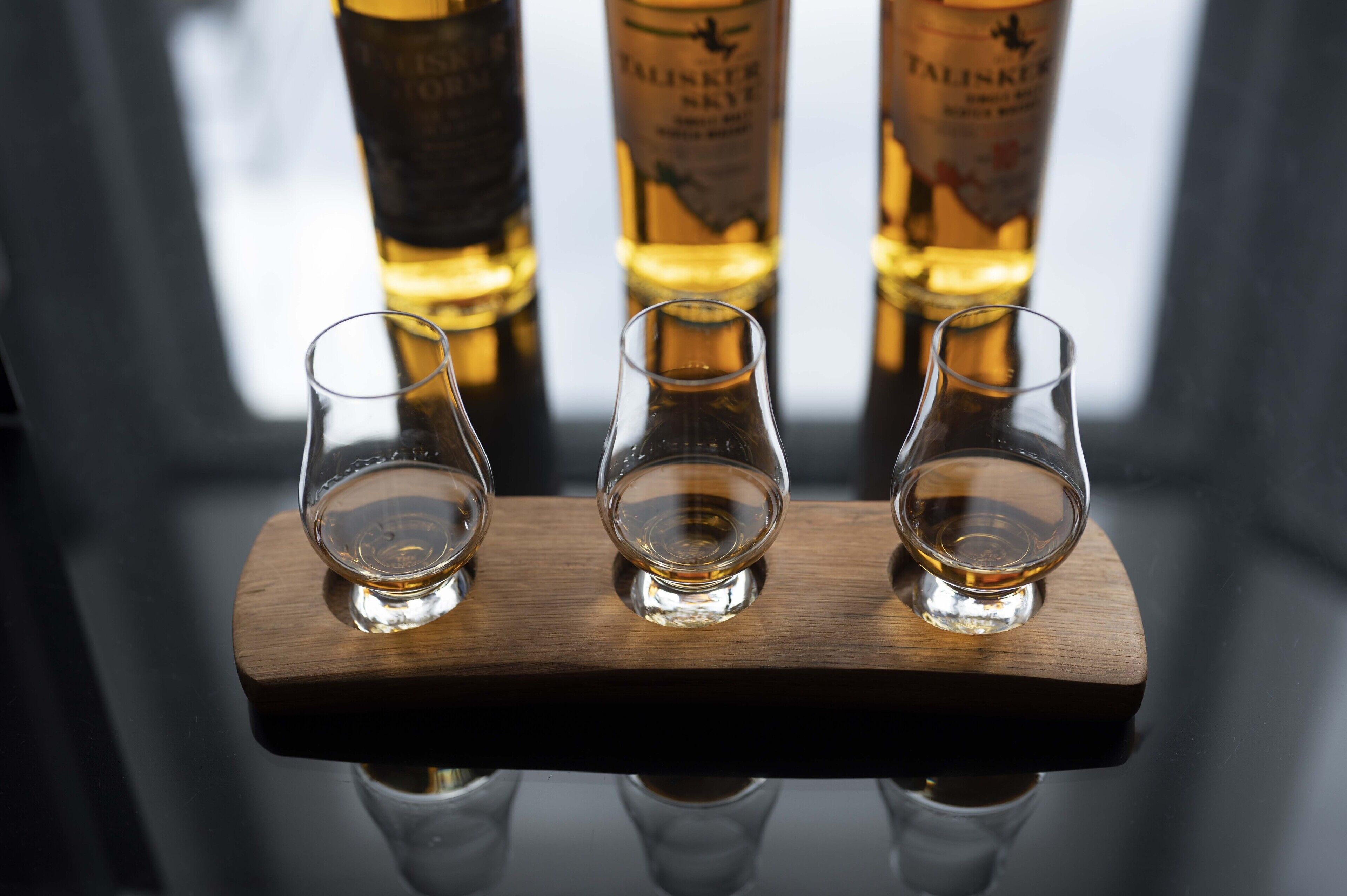 Drei leere Gläser auf einem Holzboden, mit Flaschen von Talisker im Hintergrund.