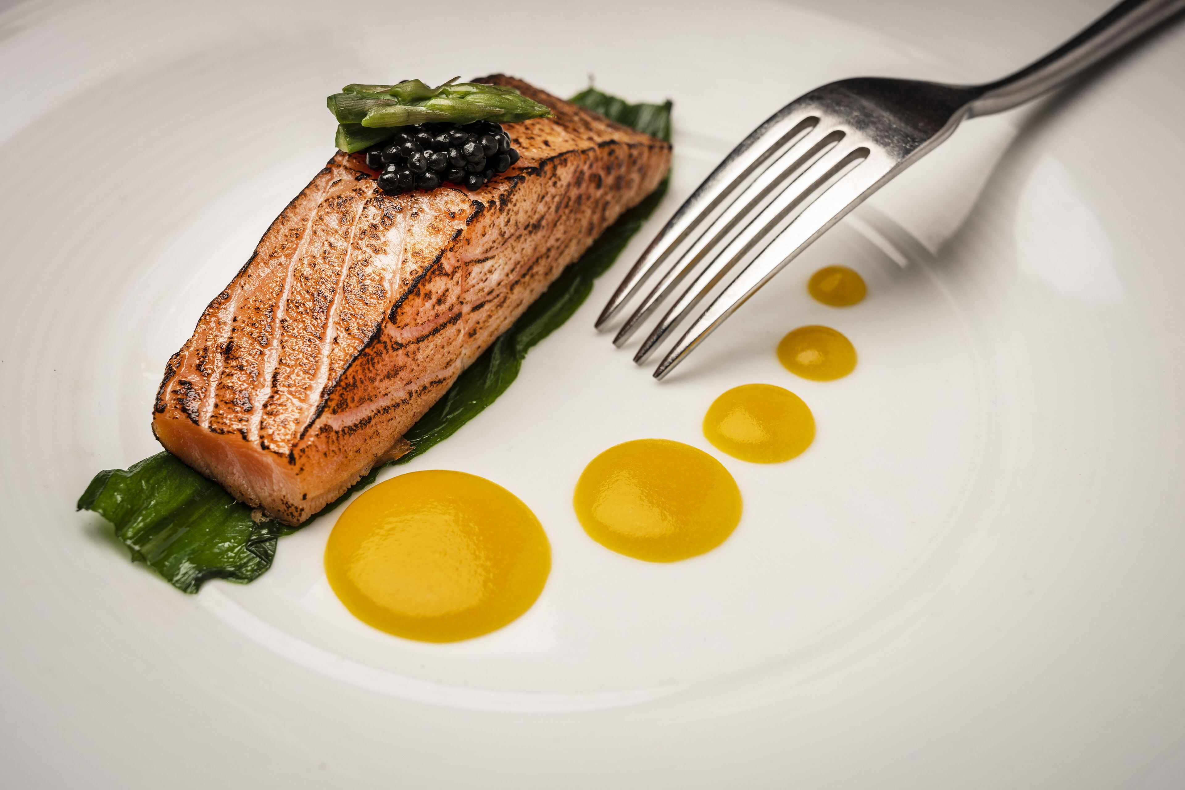 Un piatto con salmone alla griglia, asparagi e una forchetta.