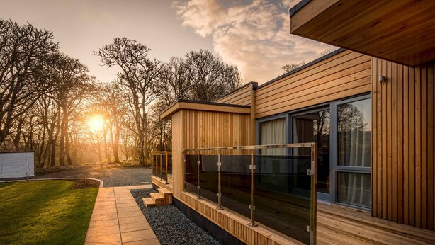 Une maison moderne en bois, dotée d’un balcon en verre, d’un chemin pavé et d’une pelouse verdoyante.