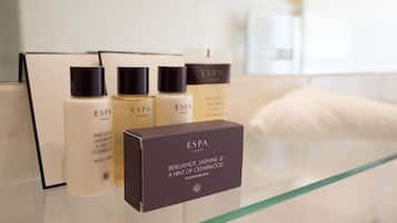 Un baño con un estante de vidrio que exhibe varios productos ESPA London, como loción corporal y jabón limpiador.