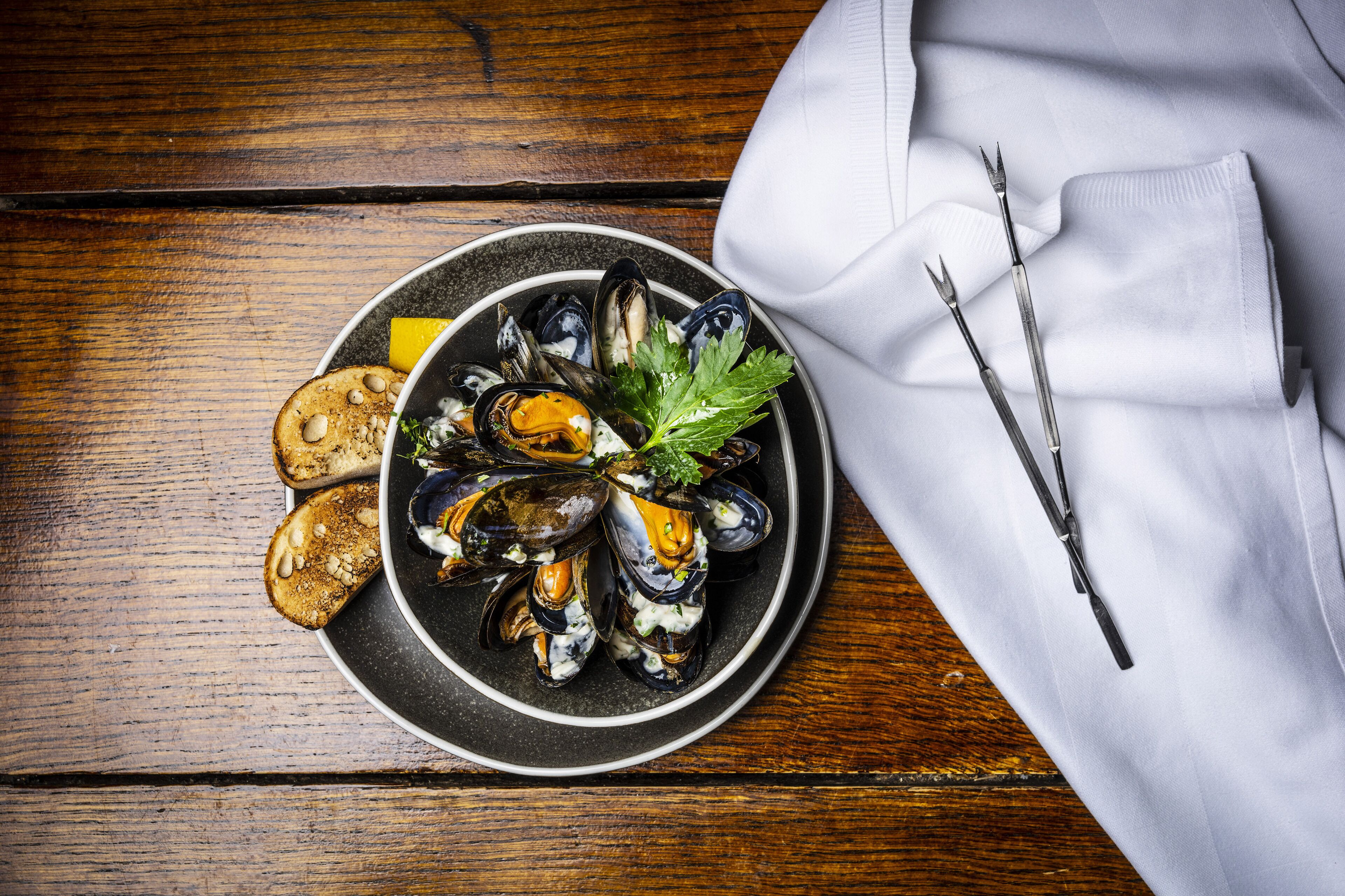 A plate of mussels with bread and parsley on a wooden table.