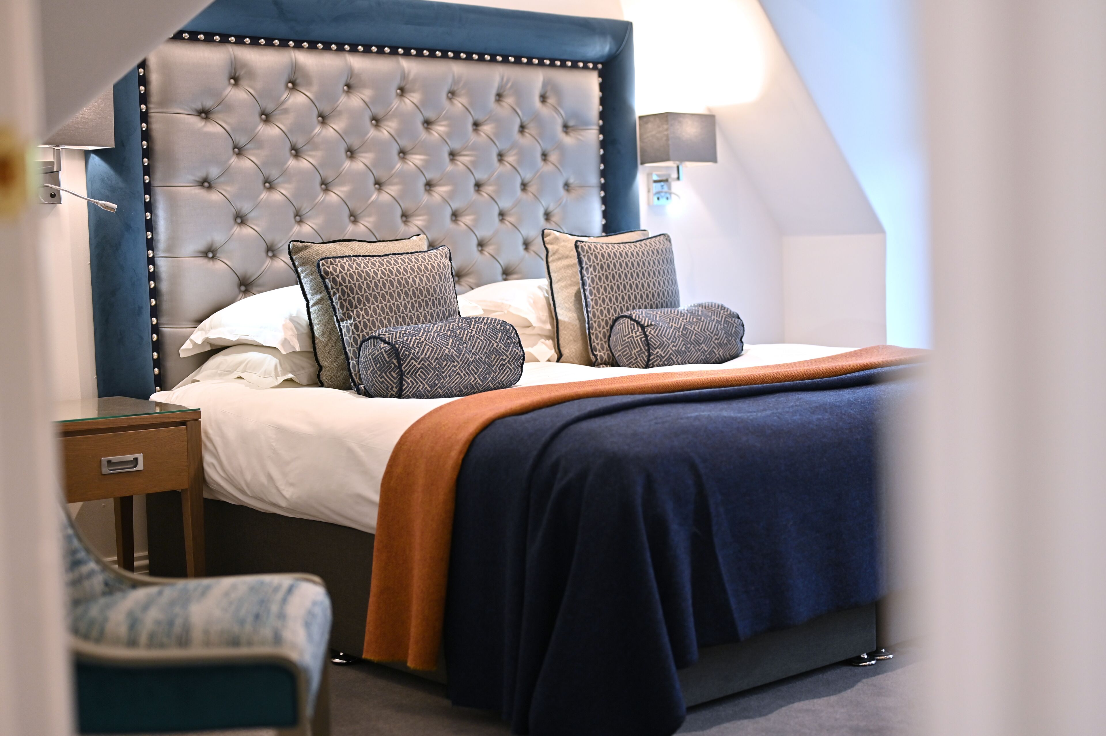 A neatly made bed with a tufted headboard, a bedside table, and a chair.