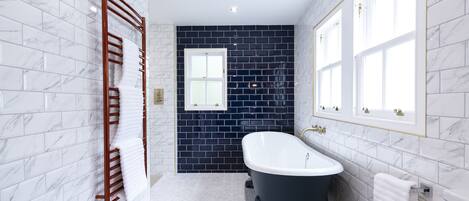 A bathroom with white marble walls, a black bathtub, and a wooden towel rack.