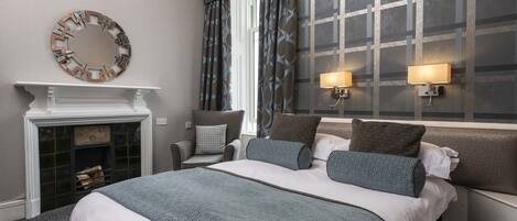 A hotel room with a large bed, a fireplace, two wall-mounted lamps, and a decorative mirror.