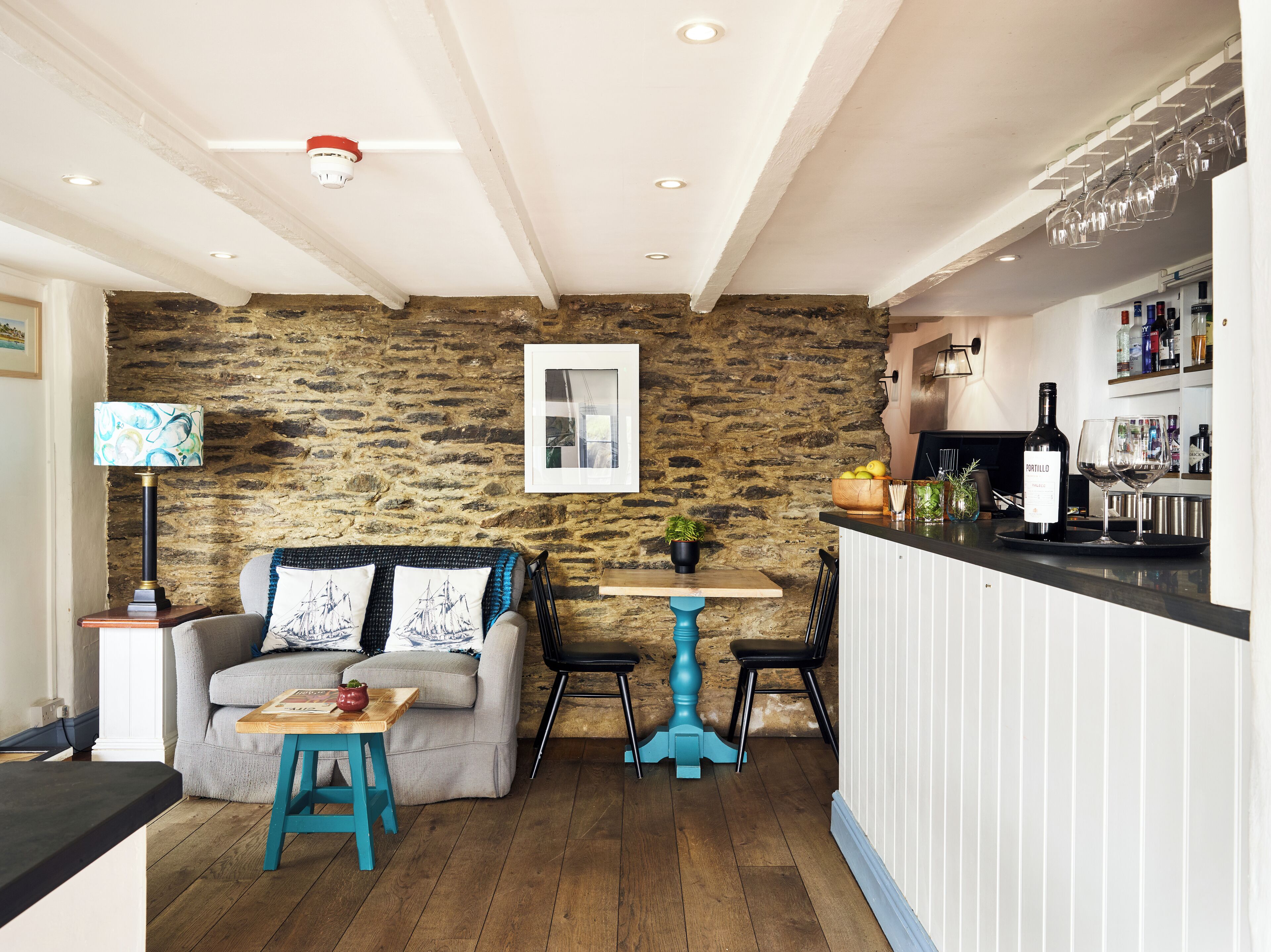 Un salon chaleureux avec un mur en pierre, une table en bois, un canapé et un coin bar avec des verres et des bouteilles de vin.
