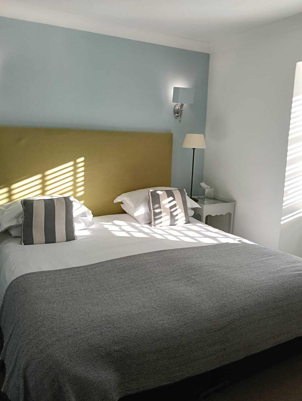 A neatly made bed with striped pillows, a grey blanket, and a yellow headboard in a room with light blue walls.