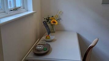 A small, white dining table with a chair, a vase with sunflowers, a small plate with an apple, and a tray with a teapot and cups.