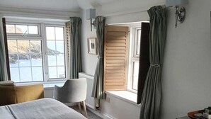 A bedroom with a large bed, a chair, a dresser, and a window with curtains. - The Lugger Hotel (Truro)