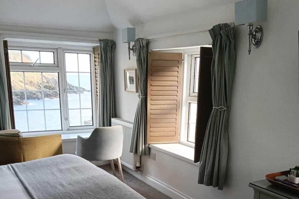 Un dormitorio con una cama grande, una silla, un aparador y una ventana con cortinas.