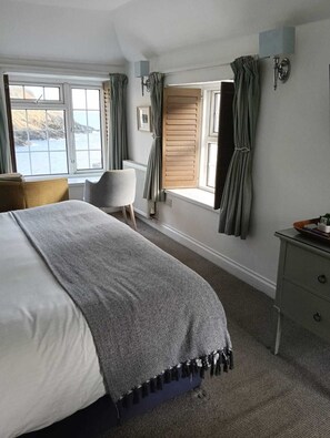 Un dormitorio con una cama grande, una silla, un aparador y una ventana con cortinas.