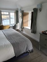 A bedroom with a large bed, a chair, a dresser, and a window with curtains.