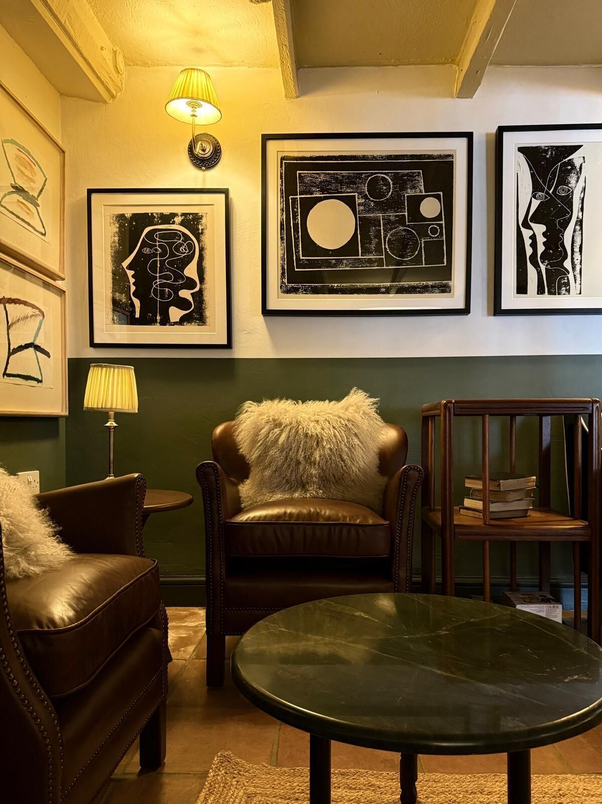 A room with a leather sofa, a round table, and framed artwork on the wall.