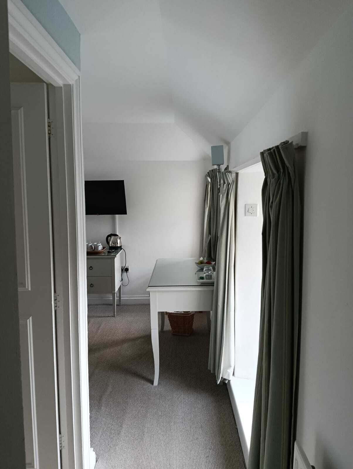 A small, neatly arranged bedroom with a single bed, a bedside table, a chair, a desk, and a television.