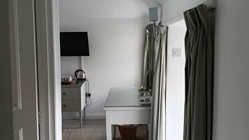 A small, neatly arranged bedroom with a single bed, a bedside table, a chair, a desk, and a television.