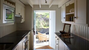 A kitchen with a view to a rocky landscape, a dining area with a chair, and a buffet setup. - The Lugger Hotel (Truro)