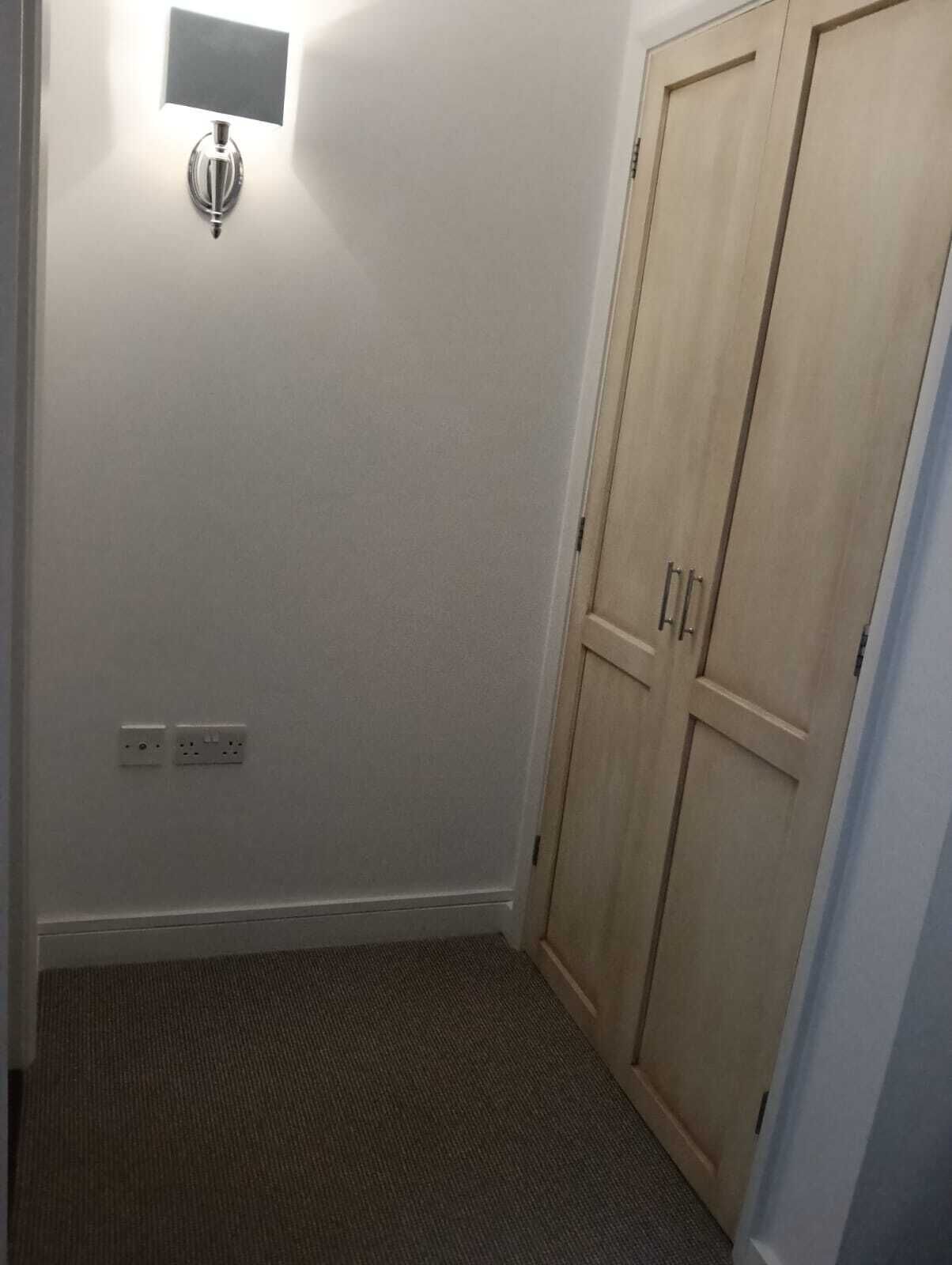Ein kleiner, schwach beleuchteter Raum mit einem Holzschrank, einem Lichtschalter und Steckdosen an der Wand.