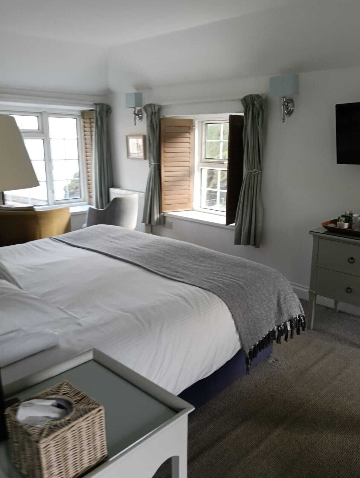 A bedroom with a bed, a chair, a bedside table, a window with curtains, and a television on the wall.