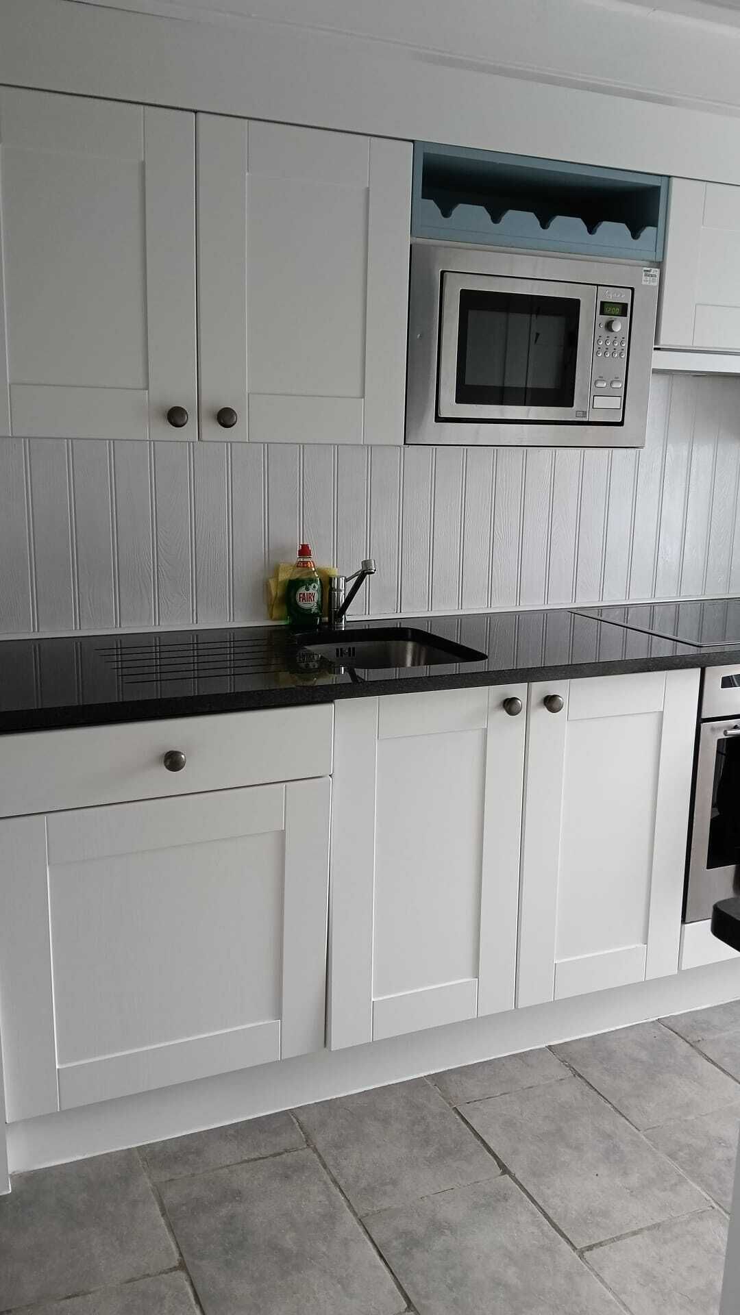 A kitchen with white cabinetry, a black countertop, a stainless steel sink, and a microwave.