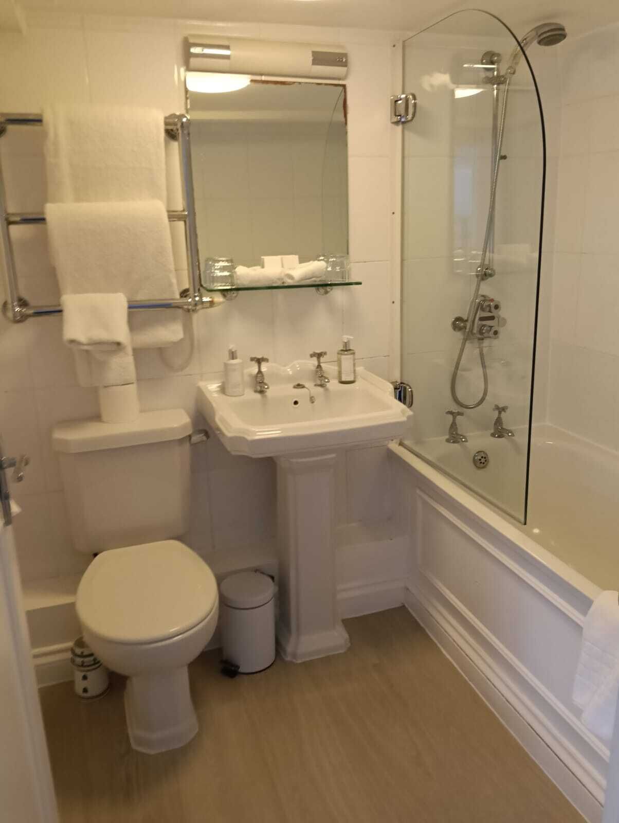 Un baño con inodoro, lavamanos y ducha con mampara de vidrio.